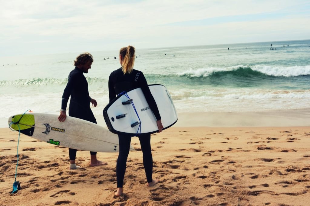 Two surfers with boards on sandy beach, ready to ride the ocean waves in sunny weather.