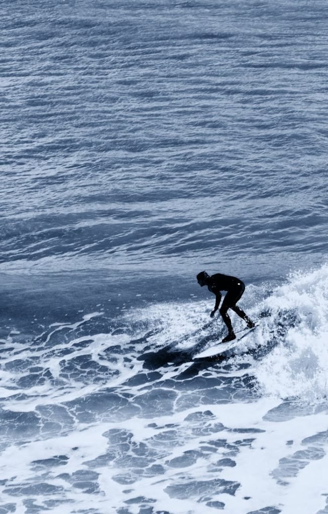 A lone surfer skillfully rides the ocean waves under a clear summer sky.
