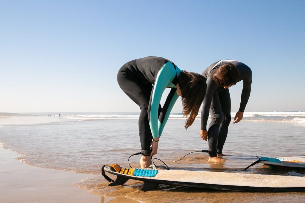 Two surfers in wetsuits preparing their boards on a sunny Portugal beach.
