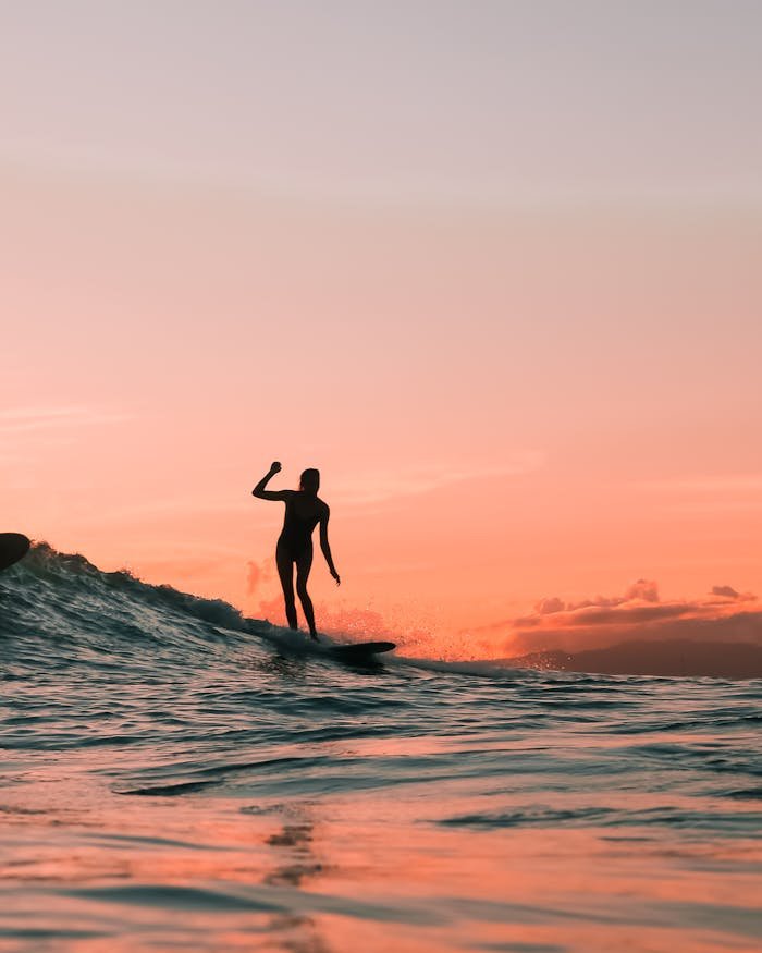 Silhouette of a surfer enjoying the waves at sunset, evoking adventure and leisure.